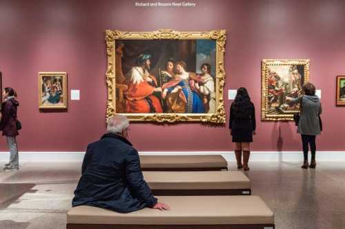 Visitors admire classic paintings in a gallery, with a large ornate artwork as the focal point.