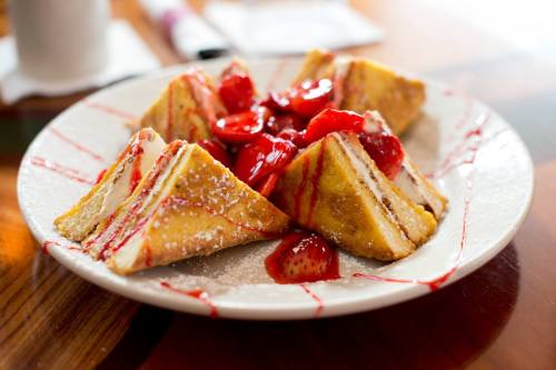 A plate of triangular French toast topped with strawberries and drizzled with syrup.