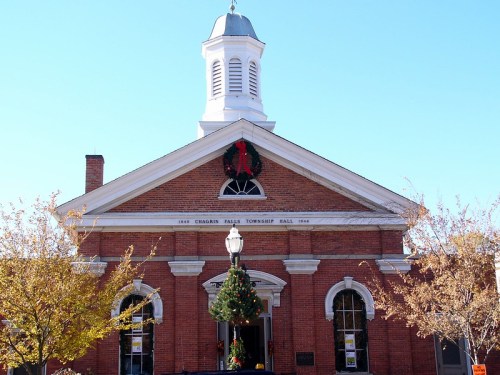 Historic brick building with a white steeple, decorated for the holidays, surrounded by trees and clear blue sky.