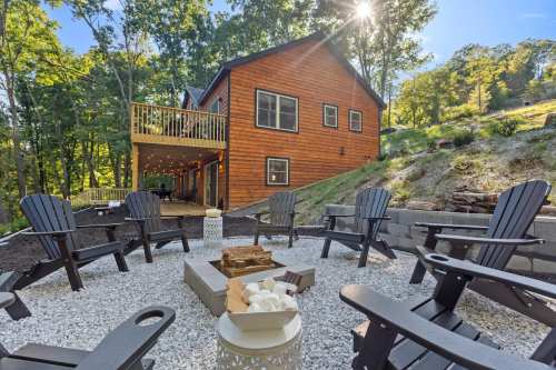 A cozy outdoor seating area with Adirondack chairs around a fire pit, set against a wooded backdrop and a cabin.