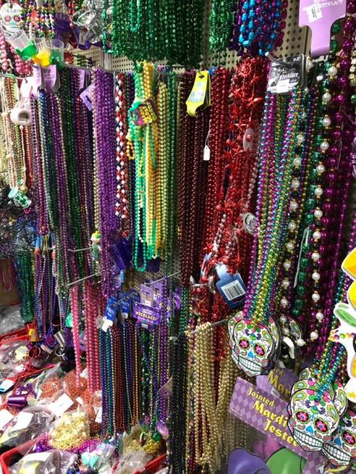 A colorful display of Mardi Gras beads in various lengths and colors, hanging on a wall.