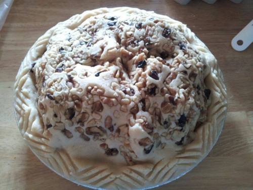 A round pie topped with a layer of nuts and a decorative crust, resting on a wooden surface.