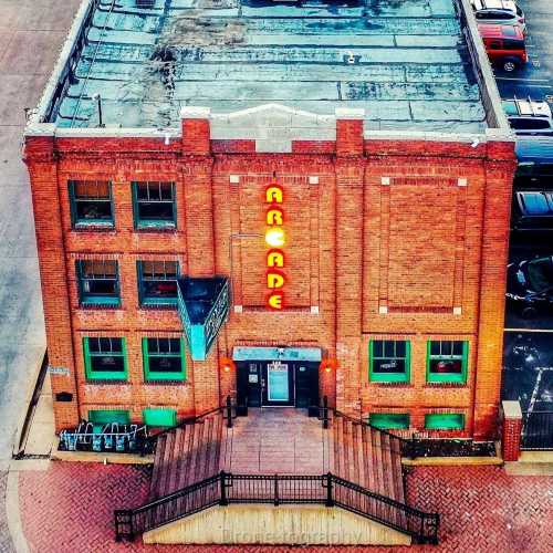 Aerial view of a brick building with "ARCADE" in neon lights, featuring green windows and a staircase entrance.