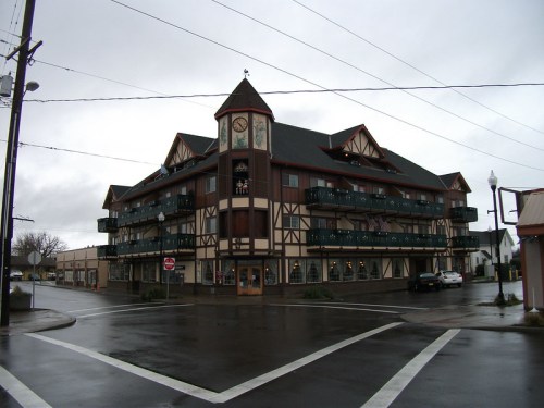A large, multi-story building with a clock tower, featuring a mix of architectural styles, on a rainy street corner.