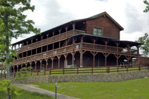 A large wooden lodge with multiple balconies, surrounded by greenery and a stone wall.