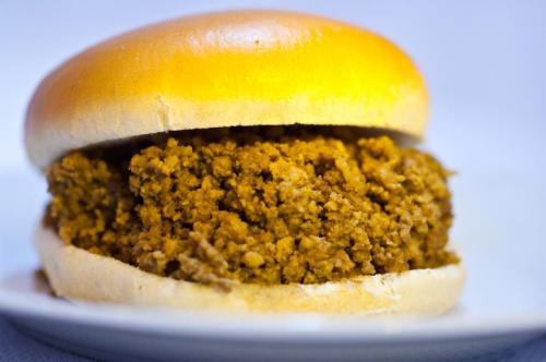A close-up of a sandwich featuring a soft bun filled with a textured, seasoned meat mixture.
