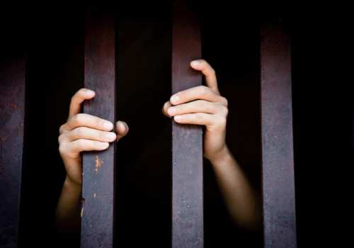 Two hands gripping metal bars, suggesting confinement or imprisonment, against a dark background.