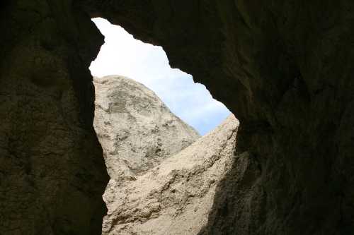 A view through a rock formation, revealing a bright sky and rugged terrain beyond.