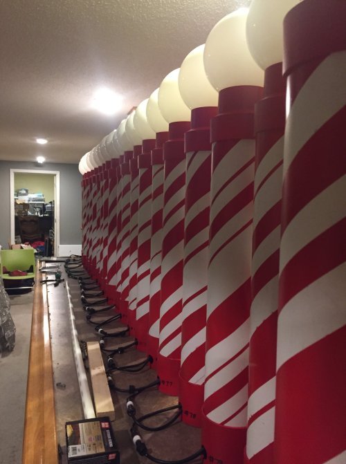 A row of red and white striped poles lined up in a dimly lit room, with tools and equipment in the background.