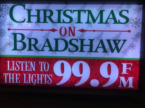 Sign promoting "Christmas on Bradshaw" with details to listen to the lights on 99.9 FM.
