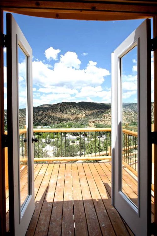 Open double doors reveal a scenic view of mountains and blue sky from a wooden deck.