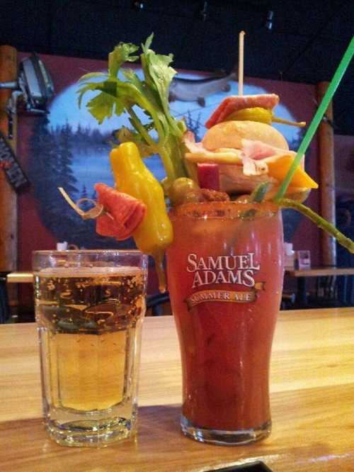 A colorful cocktail garnished with vegetables and a glass of beer on a wooden bar.