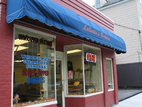 A bakery storefront with a blue awning, featuring a sign that says "OPEN" and displays various pastries in the window.