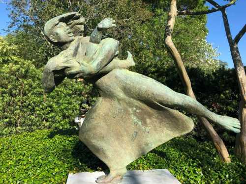 A bronze sculpture of a woman in motion, holding a child, surrounded by greenery and trees.