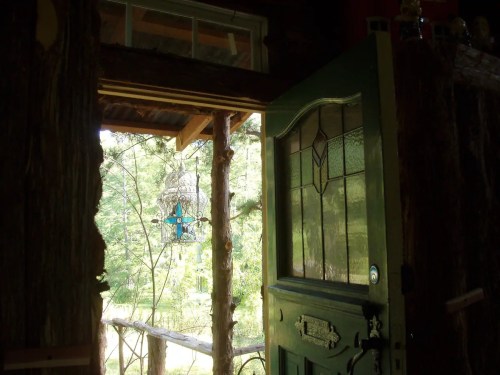 A rustic green door stands open, revealing a lush outdoor scene with trees and a hanging lantern.