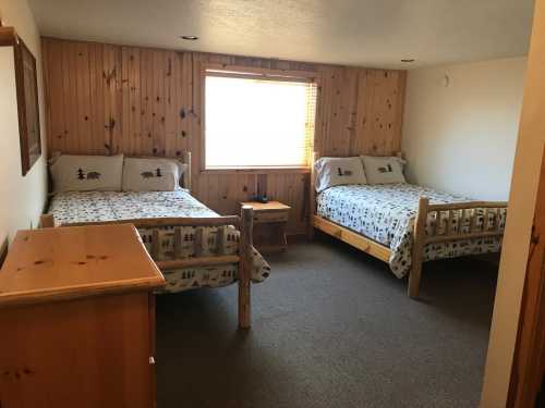 Cozy room with two wooden beds, a nightstand, and a window, featuring wooden paneling and a carpeted floor.