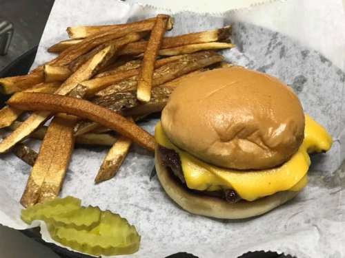 A cheeseburger with melted cheese on a bun, served with crispy fries and a pickle slice on a paper-lined tray.