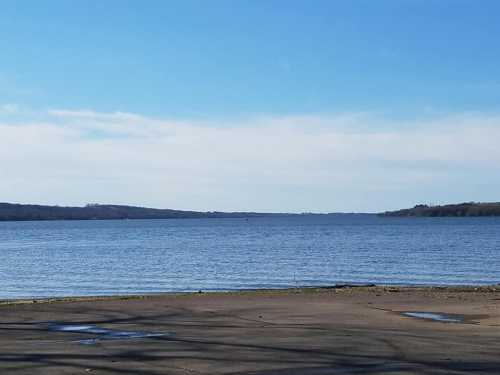 A calm lake under a clear blue sky, with distant hills visible on the horizon.