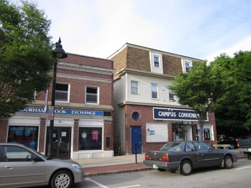 A street view of two buildings: a brick bookstore on the left and a convenience store on the right, with parked cars.