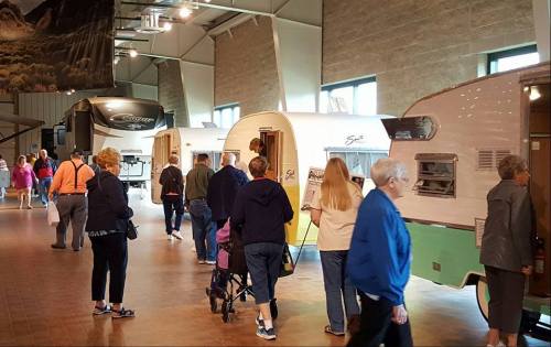 Visitors explore a display of vintage trailers in a spacious indoor exhibit.