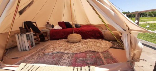 Cozy glamping tent interior with a bed, rugs, and decorative pillows, set in a serene outdoor environment.