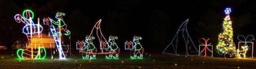 Colorful Christmas lights depicting Santa, elves, a tree, and presents in a festive outdoor scene at night.