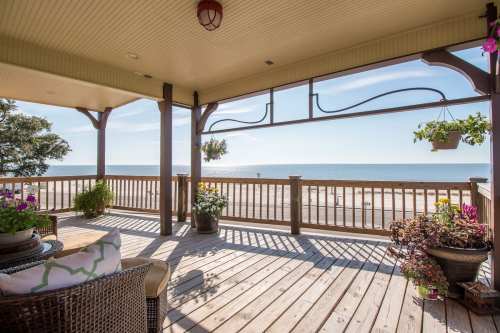 A sunny beach view from a wooden deck adorned with potted plants and comfortable seating.