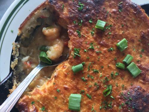 A close-up of a baked dish with shrimp, topped with green onions and herbs, served in a cast-iron skillet.