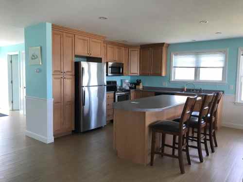 Modern kitchen with light wood cabinets, stainless steel appliances, and a large island with bar stools. Bright and airy space.