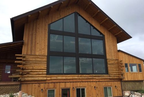 A large wooden house with a distinctive cross-shaped window and a rustic design, surrounded by natural scenery.