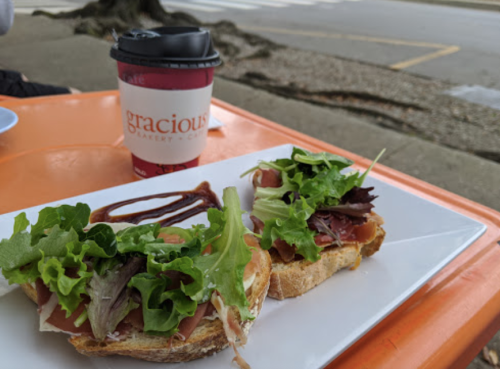 A plate with two open-faced sandwiches topped with greens, alongside a coffee cup on an orange table.
