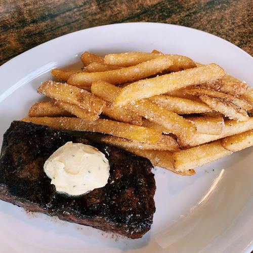 A plate featuring a grilled steak topped with herb butter, accompanied by a generous serving of golden French fries.
