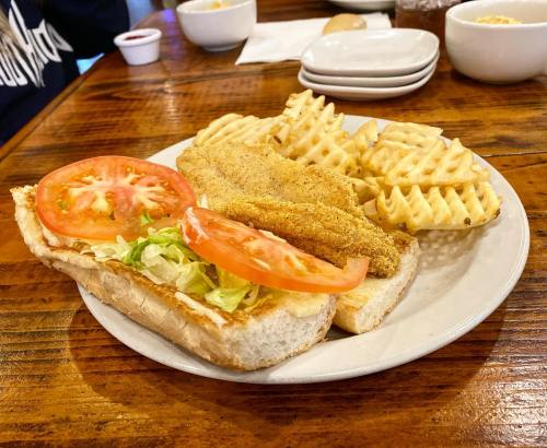 A plate with a sandwich topped with lettuce and tomato, alongside crispy waffle fries and fried fish fillets.