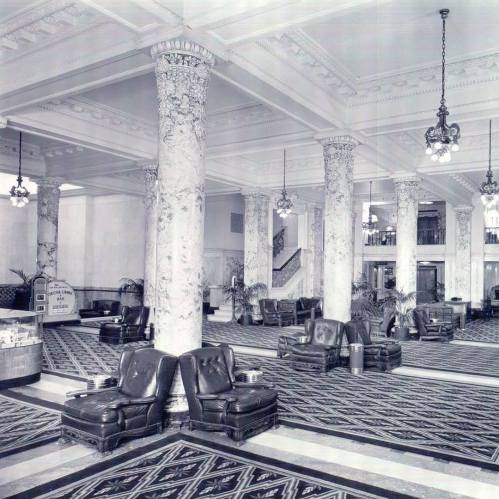 Historic lobby with ornate marble columns, vintage leather chairs, and decorative flooring, showcasing elegant architecture.