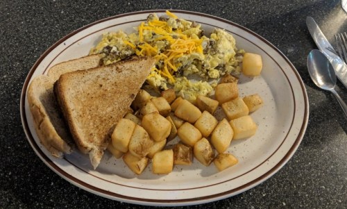 A plate of scrambled eggs with cheese, diced potatoes, and two slices of toasted bread.