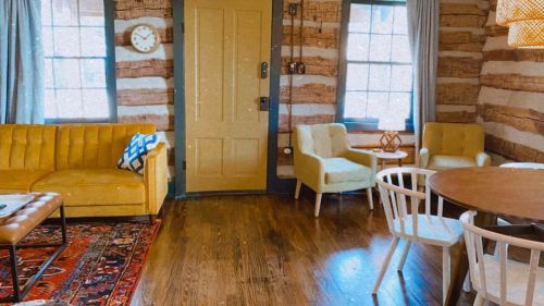 Cozy interior of a rustic room featuring a yellow couch, wooden walls, and a round dining table with chairs.