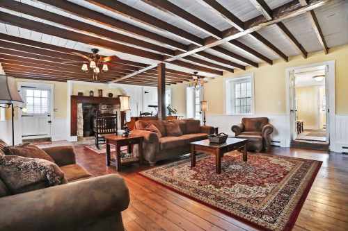 Cozy living room with wooden beams, a fireplace, comfortable seating, and warm yellow walls.