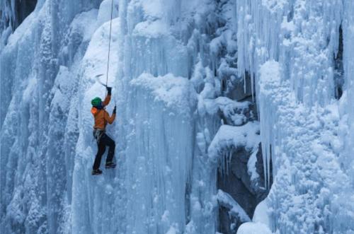 A climber ascends a frozen ice wall, surrounded by icicles and snow-covered rock.