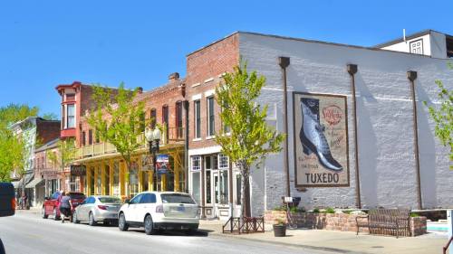 A charming street scene featuring historic buildings, parked cars, and a mural of a tuxedo cat on a white wall.