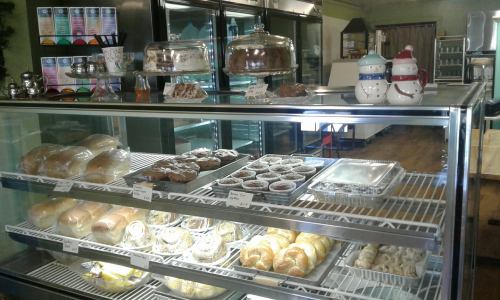 A display case filled with various baked goods, including rolls, pastries, and desserts, in a cozy bakery setting.
