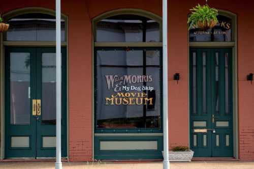 Exterior of a building featuring a sign for the "Willie Morris & My Dog Skip Movie Museum" with green doors and windows.