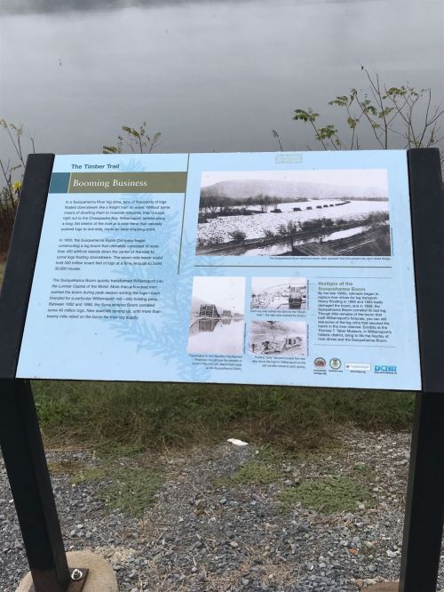 Sign about the timber industry, featuring historical photos and information, near a body of water.