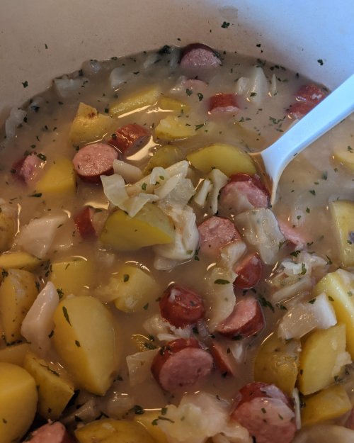 A close-up of a hearty dish featuring potatoes, sausage, cabbage, and herbs in a creamy broth.
