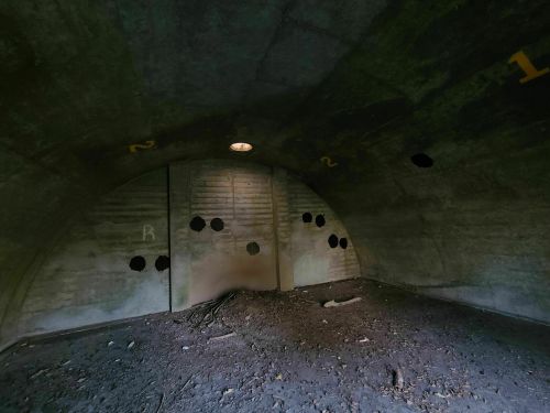 Interior of a dimly lit, abandoned concrete structure with numbered walls and dark circular marks.