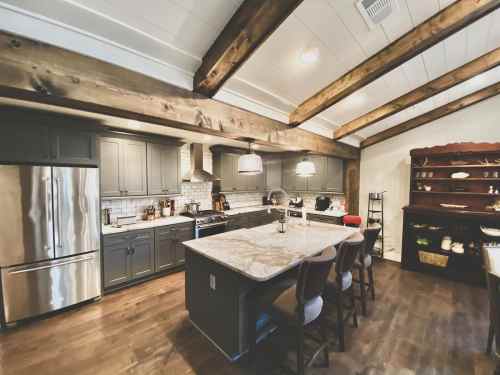 Modern kitchen with gray cabinets, a marble island, wooden beams, and stainless steel appliances. Cozy and stylish design.
