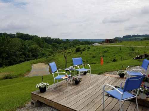 A wooden deck with blue chairs overlooks a green landscape and winding path under a cloudy sky.