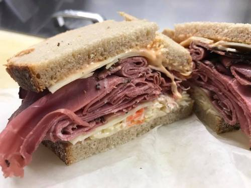 Close-up of a sandwich with layers of deli meats and condiments between slices of brown bread.