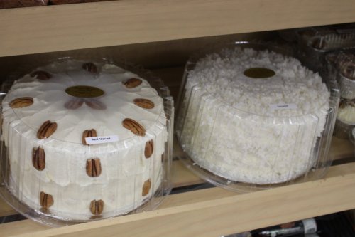 Two round cakes in clear packaging on a shelf: one with pecans and a white frosting, the other covered in coconut.