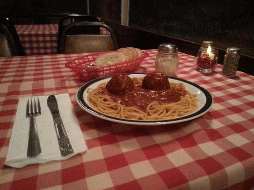 A plate of spaghetti with meatballs in marinara sauce, served on a checkered tablecloth with bread and condiments nearby.