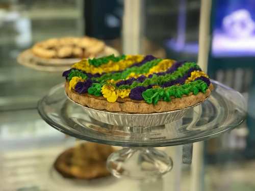 A colorful pie with green, purple, and yellow frosting, displayed on a glass cake stand in a bakery.